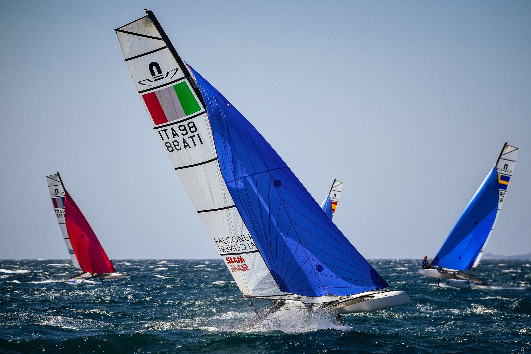 Catamarano Nacra 17 con spinnaker blu in navigazione con vento forte, altre barche sullo sfondo