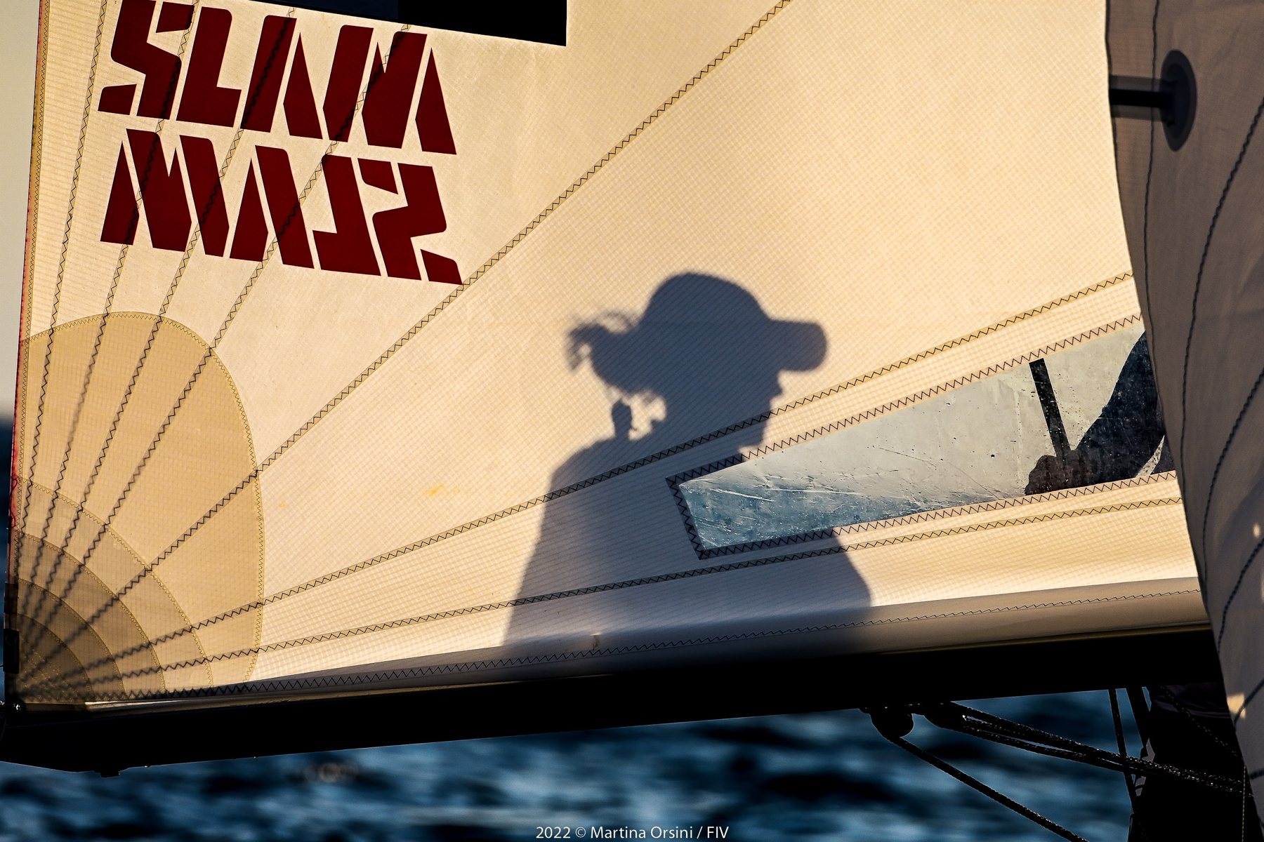 Ombra di una persona proiettata sulla randa di un catamarano al tramonto