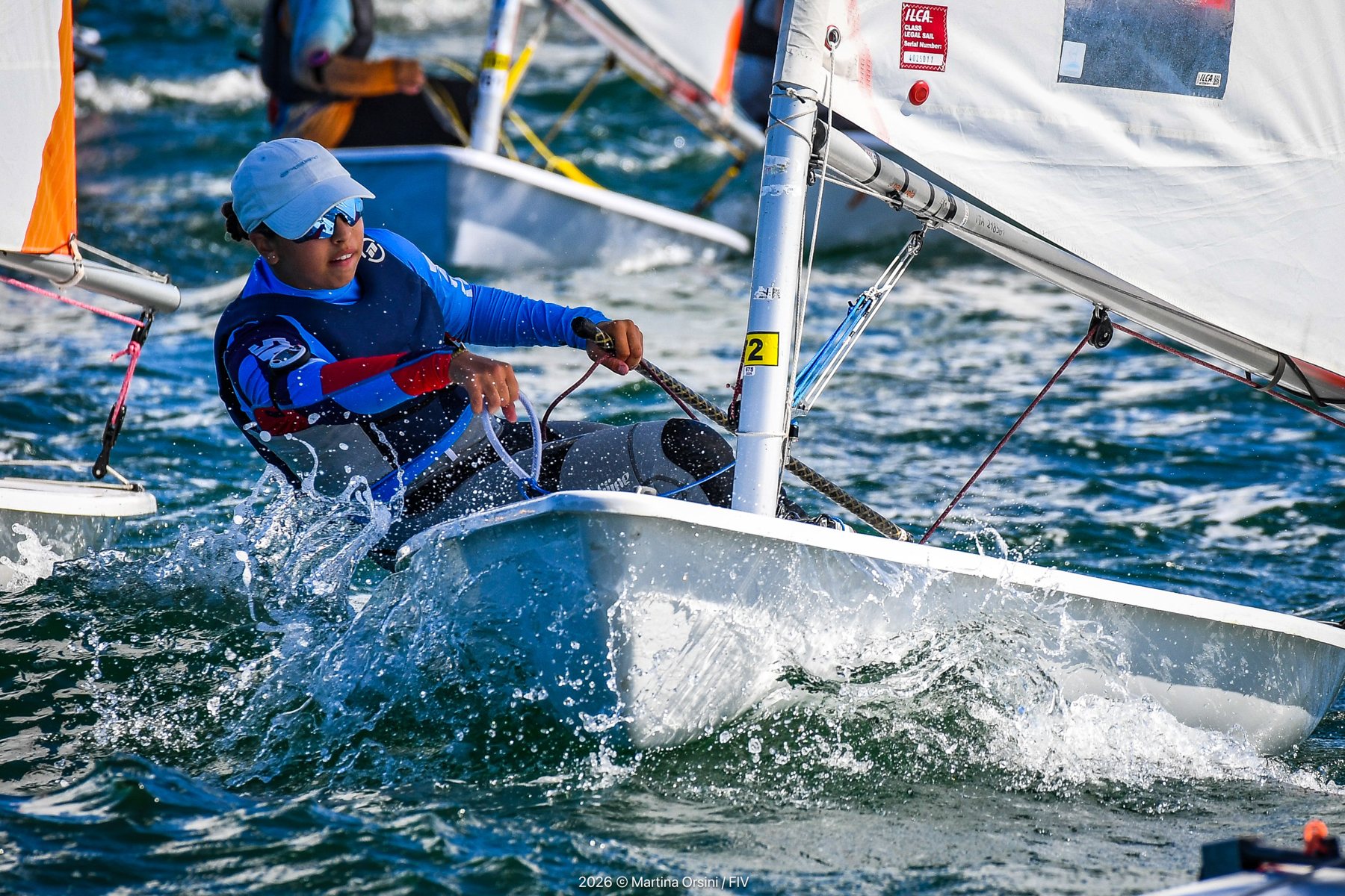 Velista in Optimist con spruzzi d'acqua mentre regola la vela