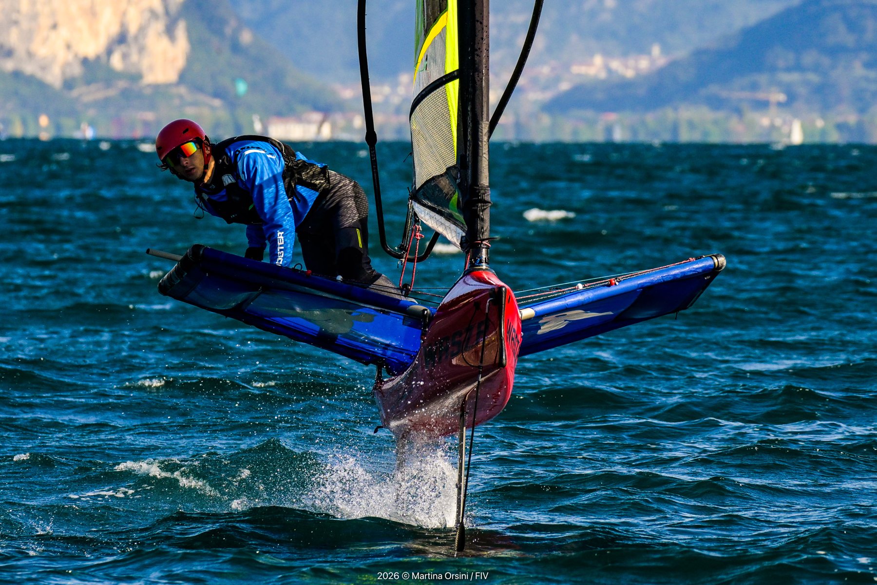 Velista su una barca foil in volo sopra l'acqua con montagne sullo sfondo